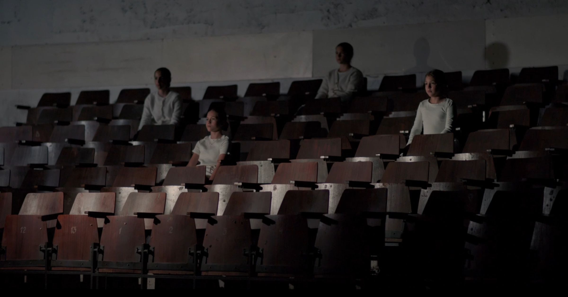 Four girls in white sit apart in an empty old cinema hall, a still from Somebody Missing