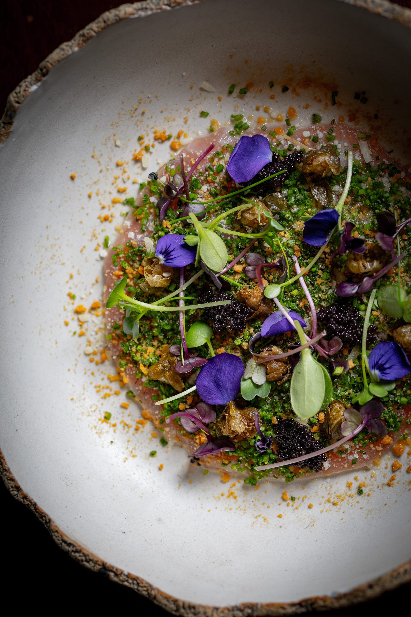 Carpaccio with violet petals and caviar in a stoneware bowl