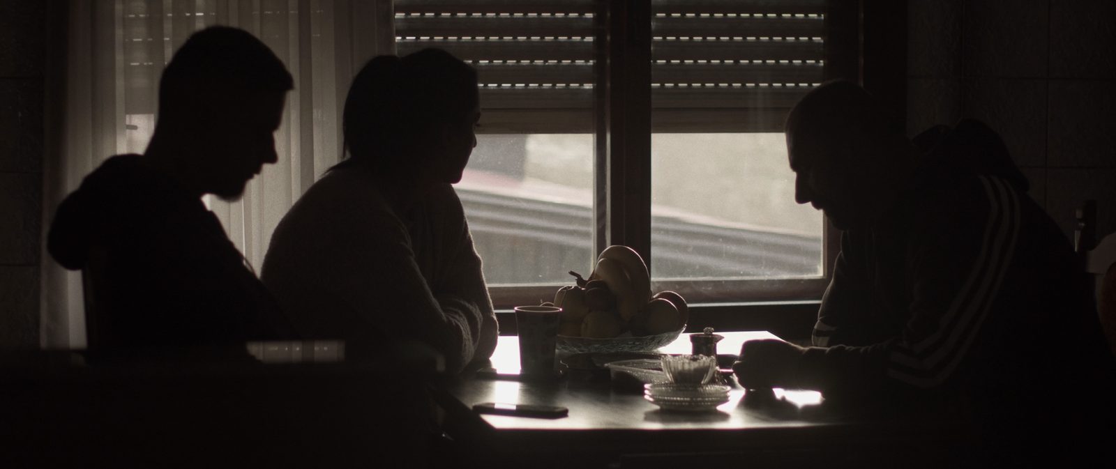 Three people in silhouette at a kitchen table against a window